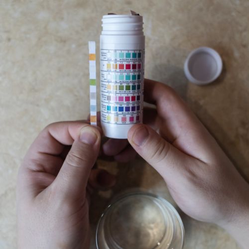 Person holding a pH test kit with a color chart on a beige surface